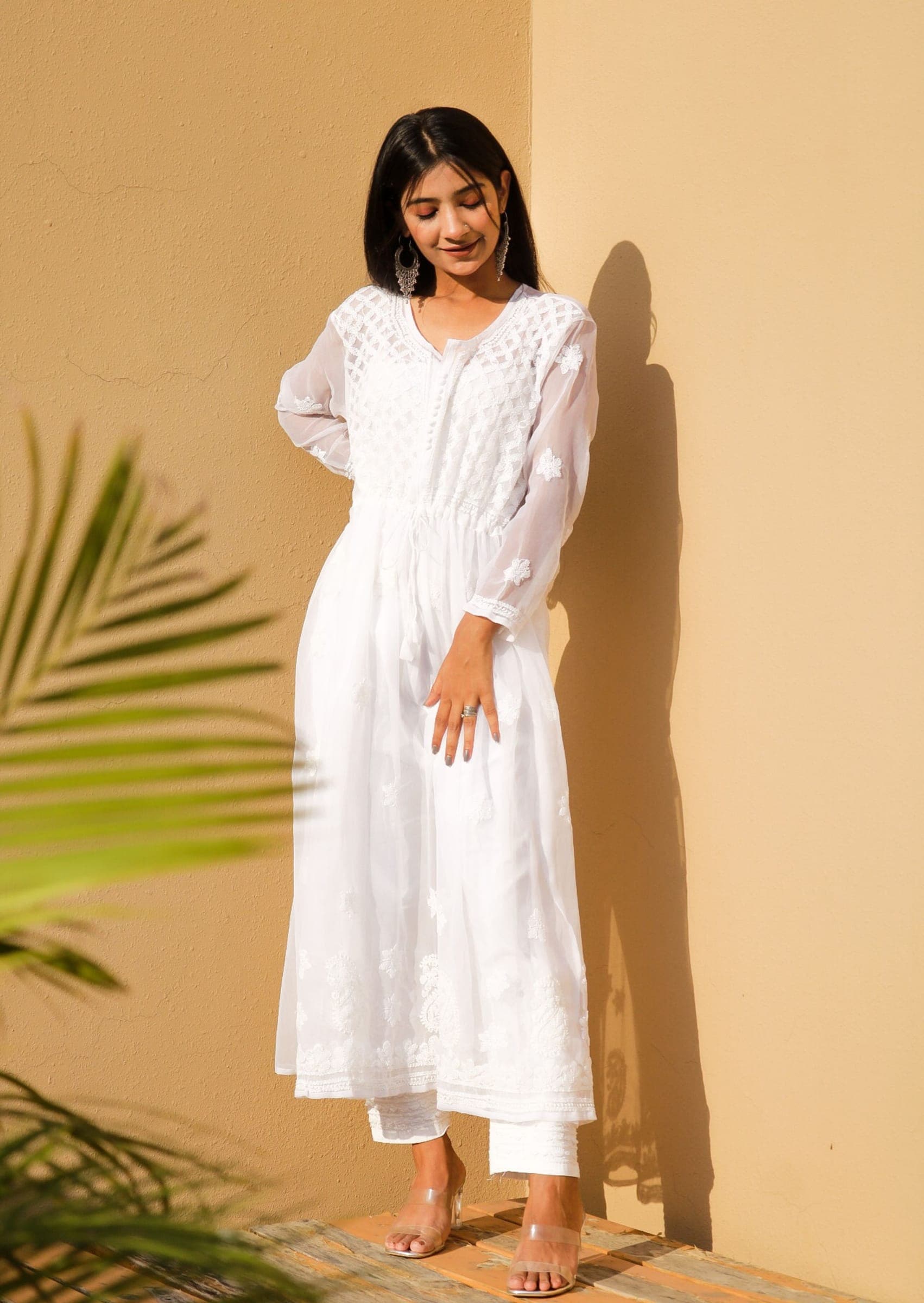 Woman in a white chikankari cotton kurta set standing against a warm wall in sunlight